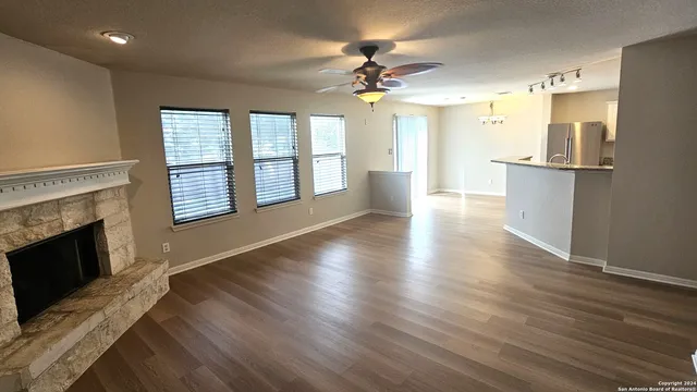 a view of an empty room with wooden floor and a kitchen
