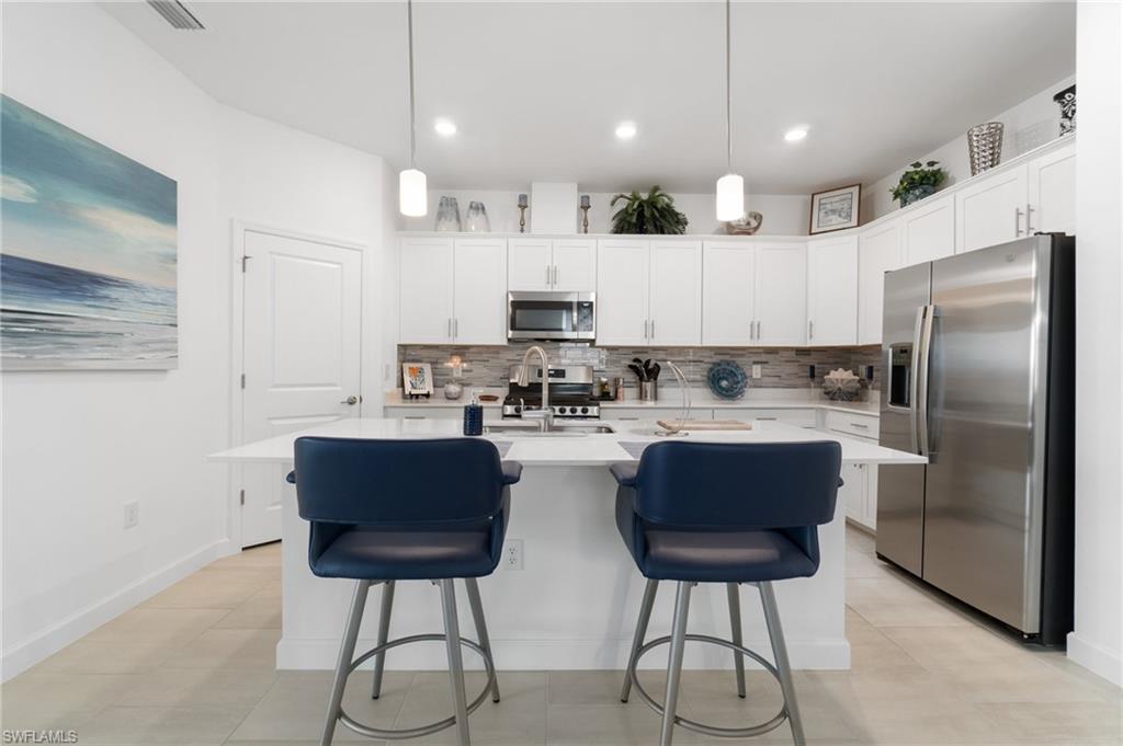 20238 Millrun Drive Estero, FL 33928 - Photo 15 of 41 a kitchen with stainless steel appliances granite countertop a refrigerator a stove a sink and chairs with wooden floor