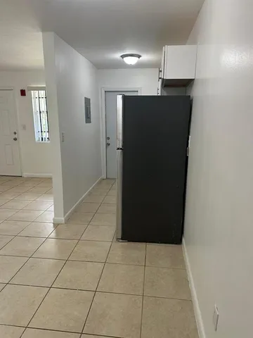 a view of a refrigerator in kitchen and an empty room in wooden floor