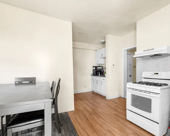 a kitchen with a stove and white cabinets with wooden floor