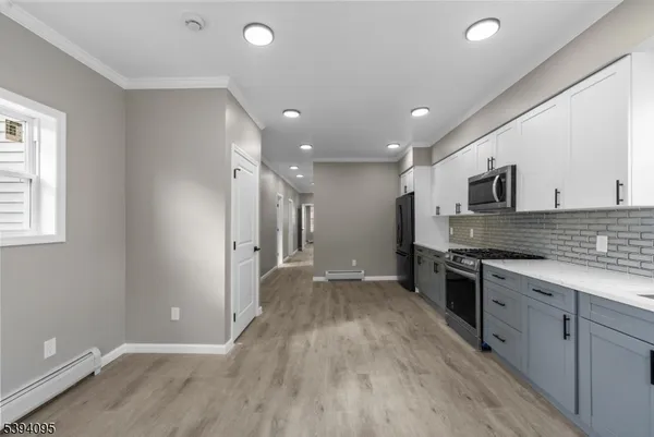 a large kitchen with stainless steel appliances a large counter top a stove a sink and a refrigerator with wooden floor