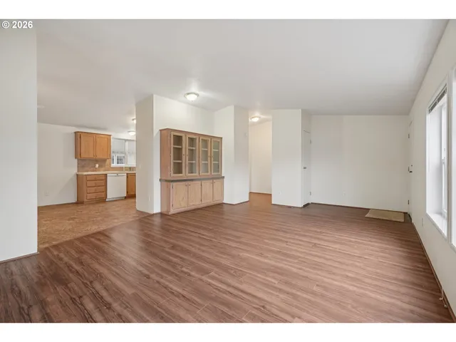 a view of empty room with wooden floor and kitchen view