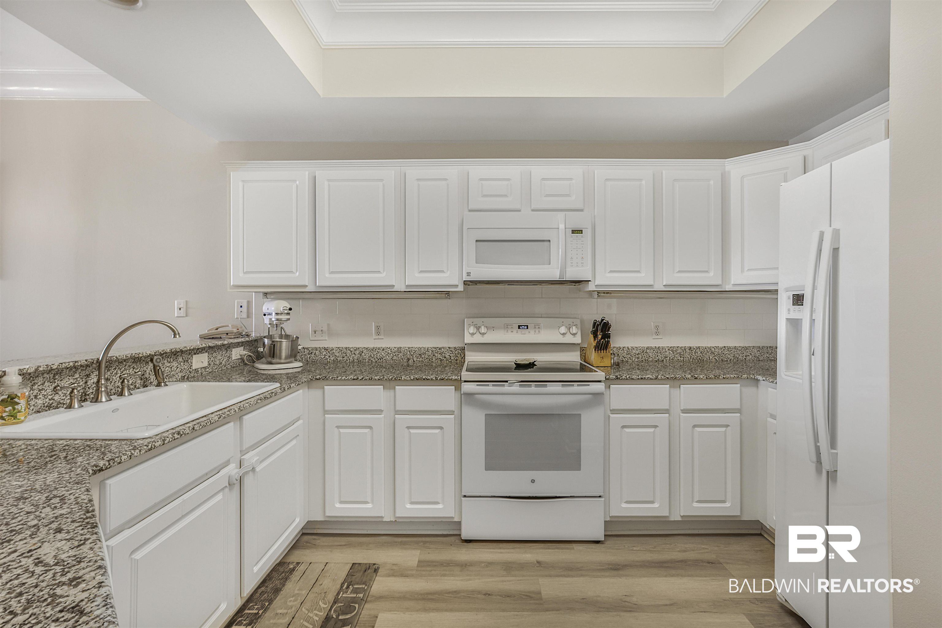 Kitchen featuring white appliances, white cabinetry, light wood finished floors, decorative backsplash, and dark stone countertops