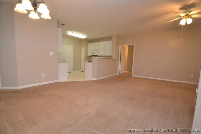 en empty room with a chandelier fan and kitchen view