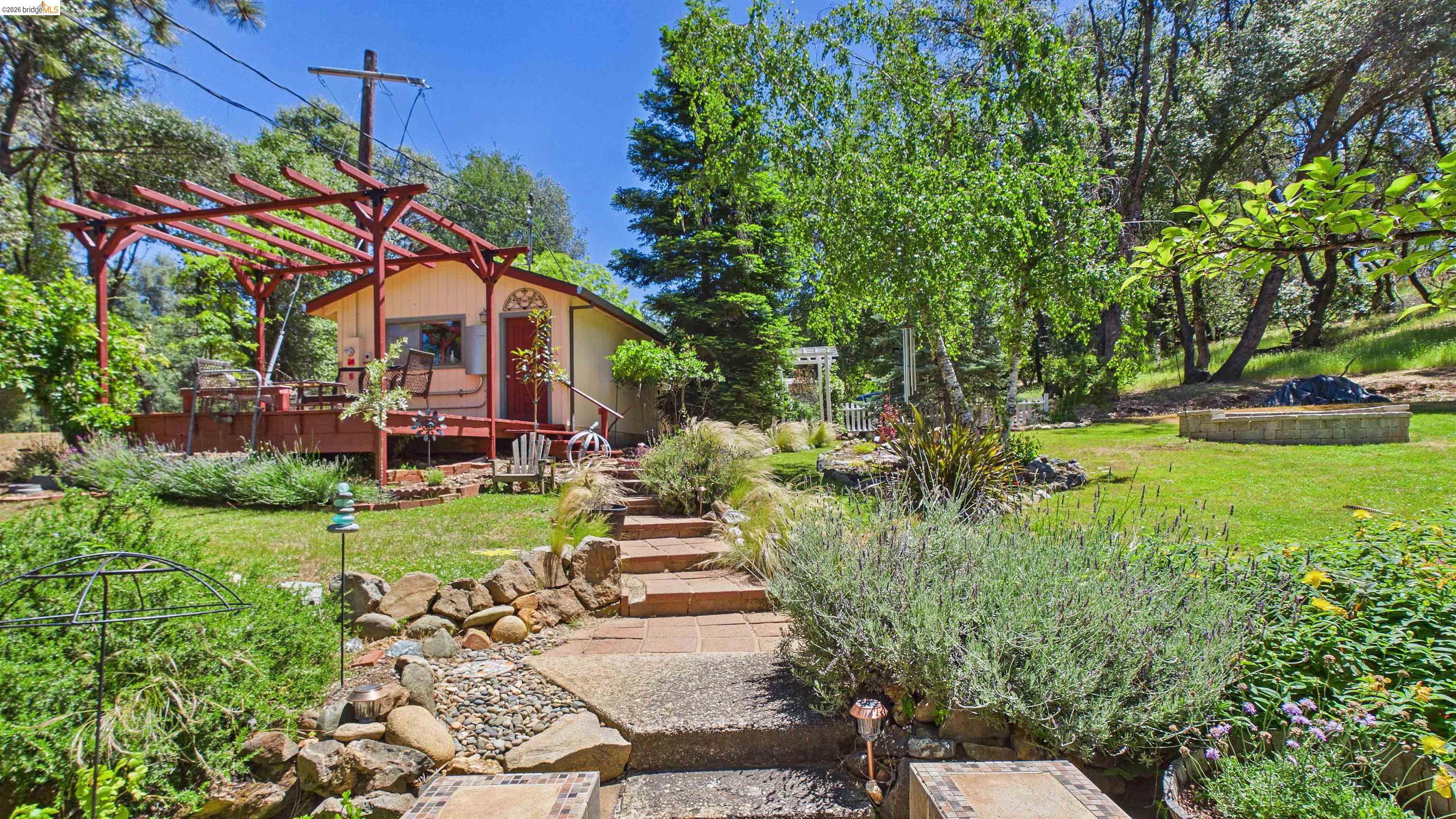 18102 Mt Eaton Road Tuolumne, CA 95379 - Photo 30 of 44 Charming exterior featuring a light-colored facade, red-stained deck with a pergola, and an arched entryway