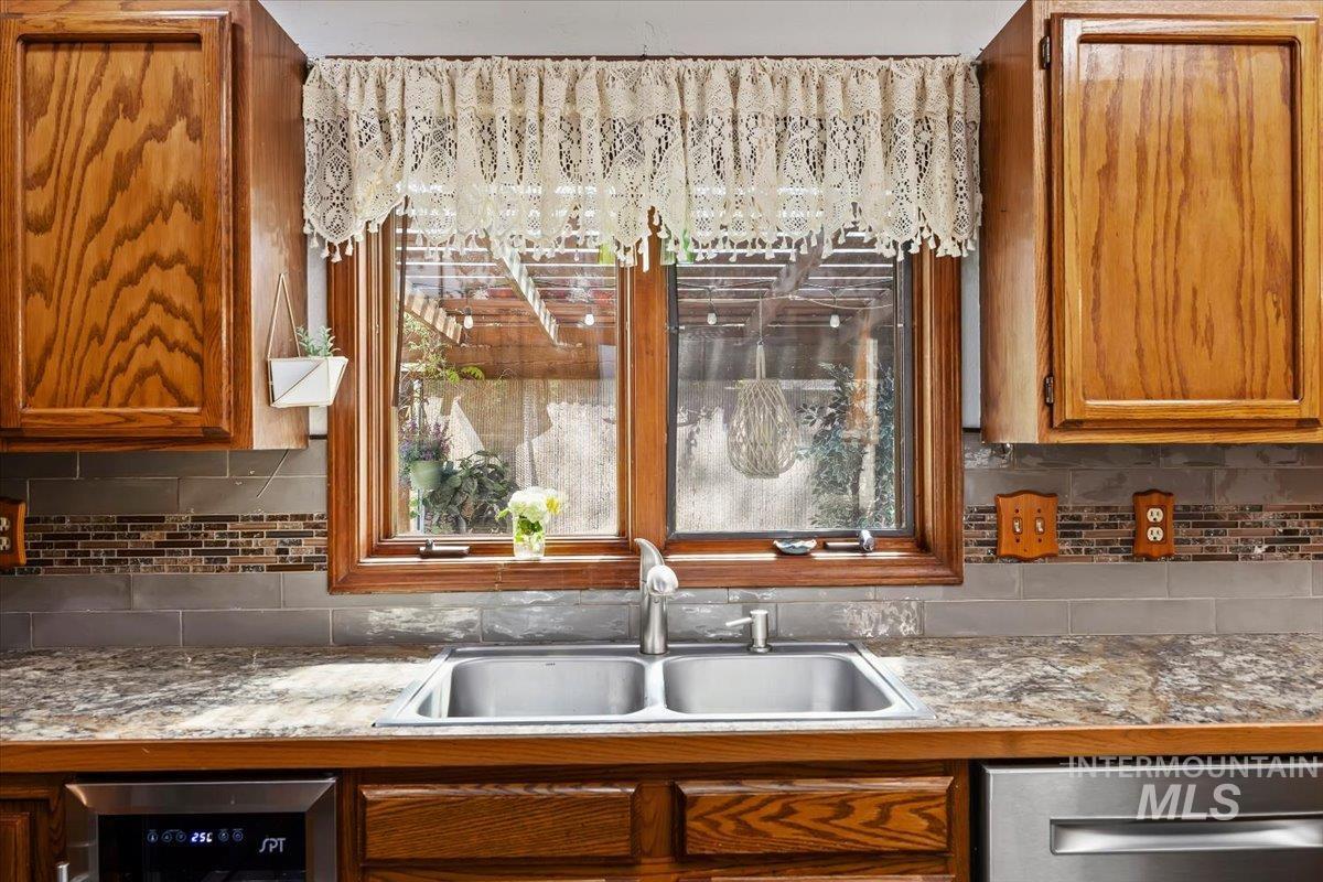 956 Bitterroot Place Twin Falls, ID 83301 - Photo 12 of 48 Kitchen sink area featuring a dual-basin stainless steel sink, wood-finish cabinetry, a patterned laminate countertop, and a tiled backsplash with mosaic accents