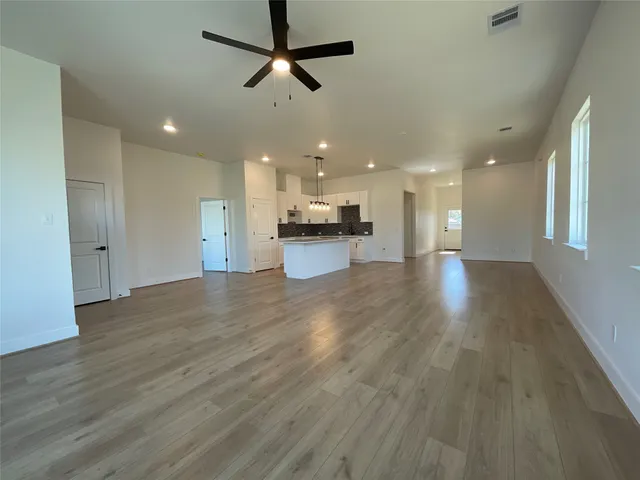 a view of a big room with wooden floor a ceiling fan and kitchen view