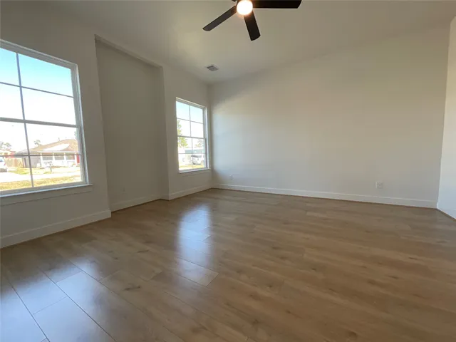 an empty room with wooden floor fan and windows