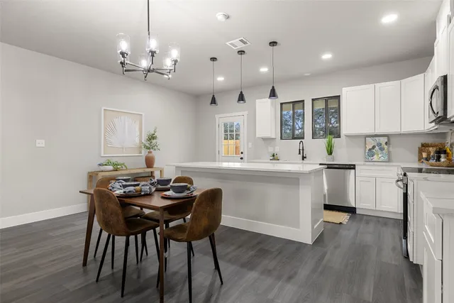a kitchen that has a table chairs in it wooden floors and white cabinets