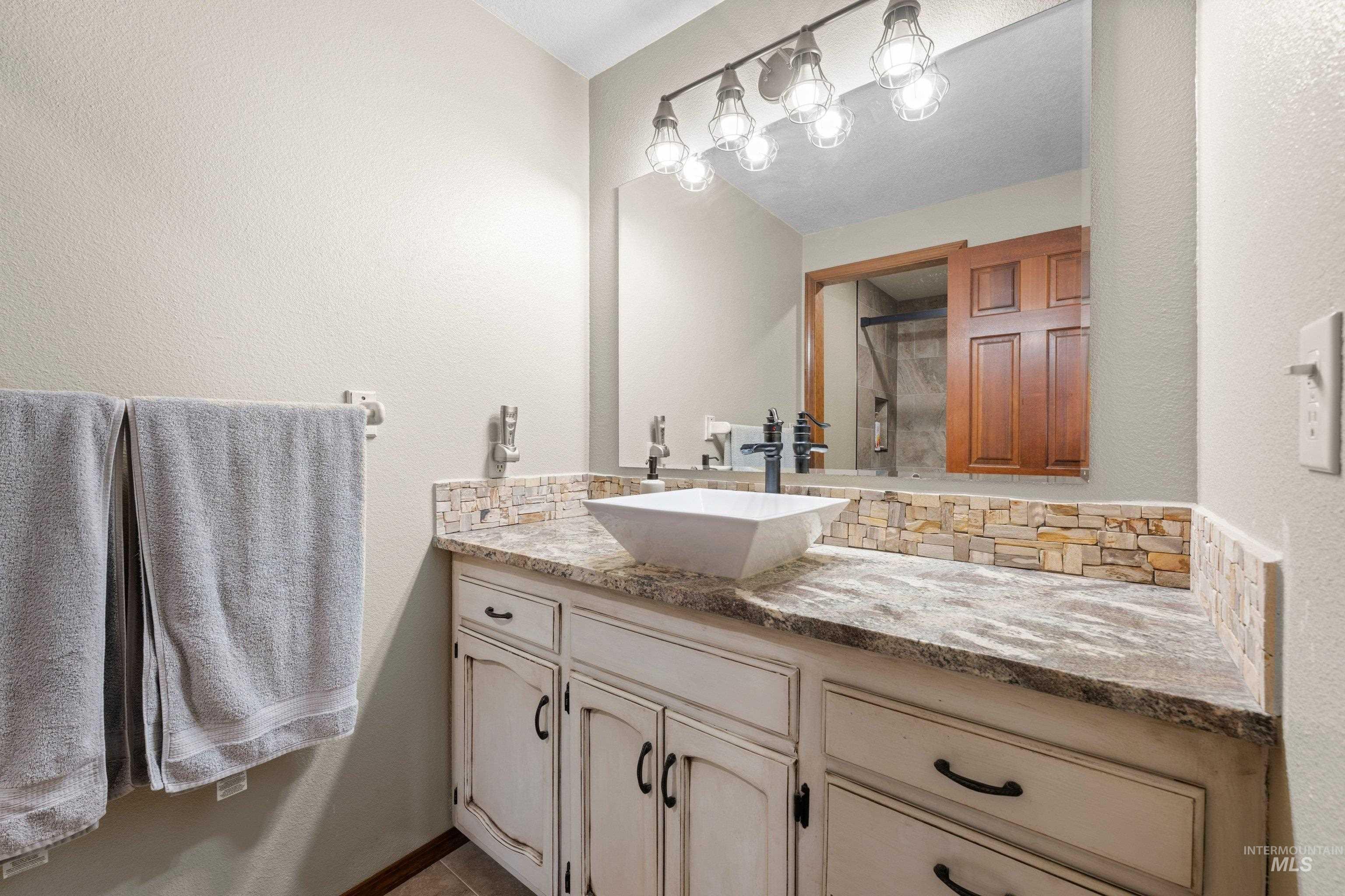 1921 Incline Way Meridian, ID 83646 - Photo 29 of 50 Bathroom vanity featuring a vessel sink with a dark-finish faucet, stone-look countertop, and a stacked stone backsplash