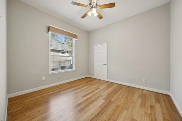 an empty room with wooden floor chandelier fan and windows