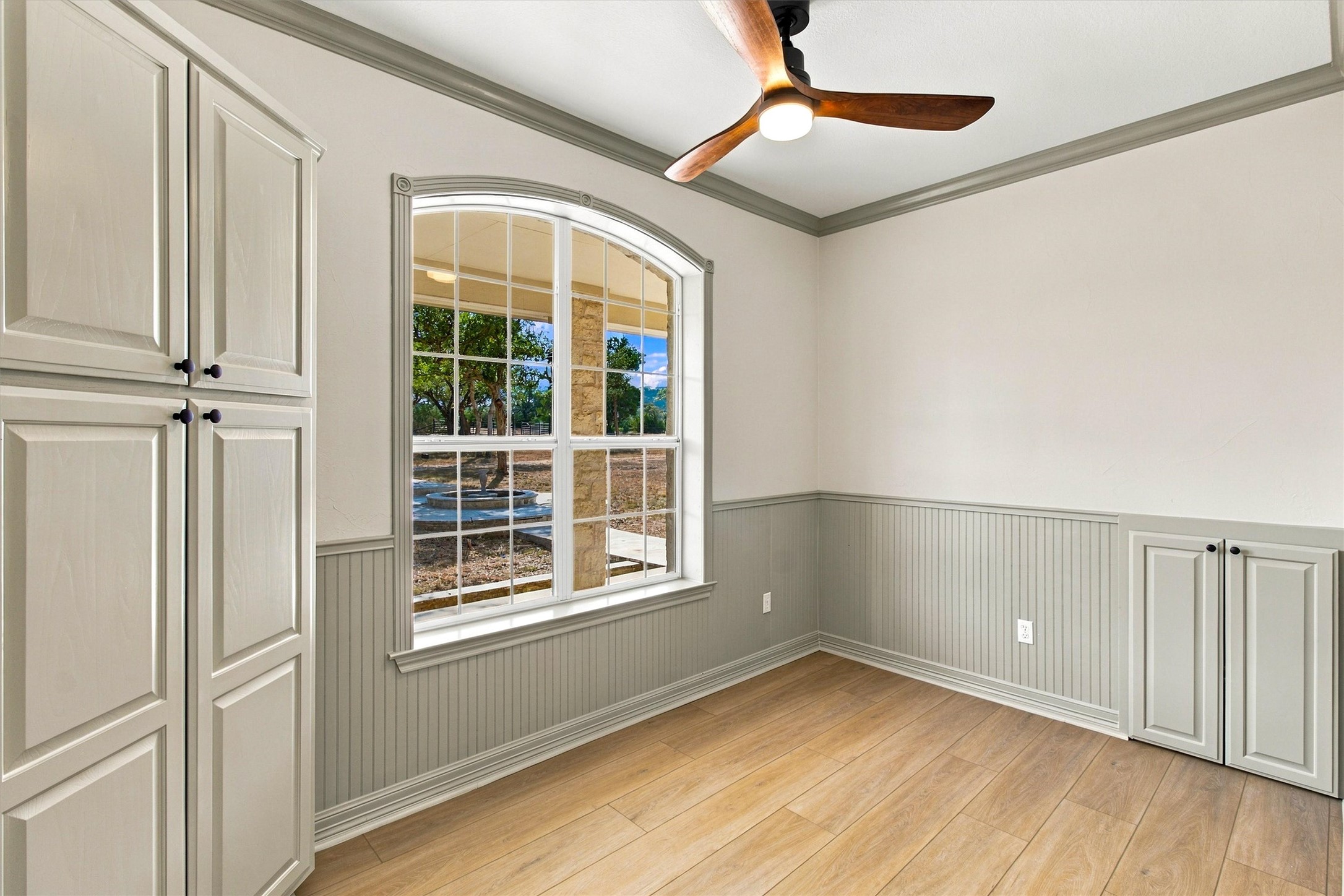 1651 Old Red Ranch Road Dripping Springs, TX 78620 - Photo 14 of 31 An arched window frames serene outdoor views, complemented by classic wainscoting and warm wood floors.