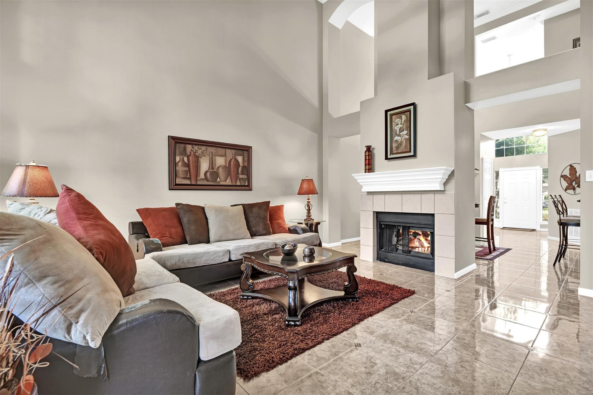 14420 Walters Road, Unit 16 Houston, TX 77014 - Photo 9 of 27 This spacious living room features high ceilings, a cozy fireplace, and elegant tile flooring. The open layout leads to a dining area, creating a welcoming and connected space.