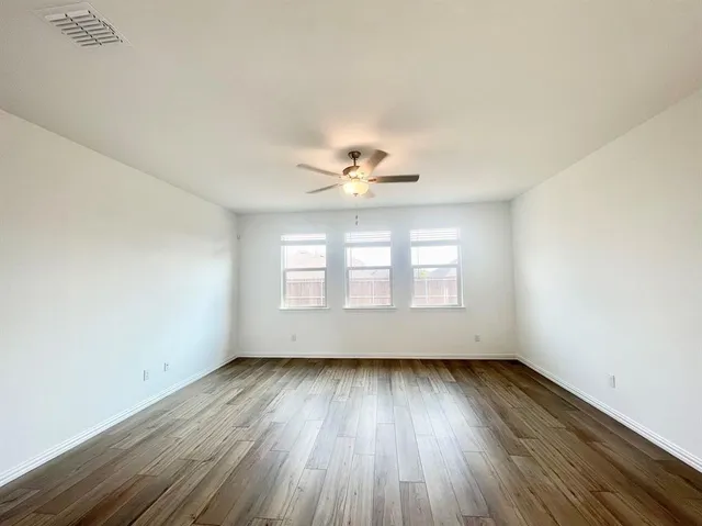 an empty room with wooden floor a ceiling fan and windows