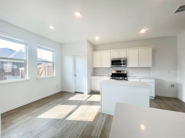 a kitchen with stainless steel appliances granite countertop a stove a sink a refrigerator white cabinets and a refrigerator