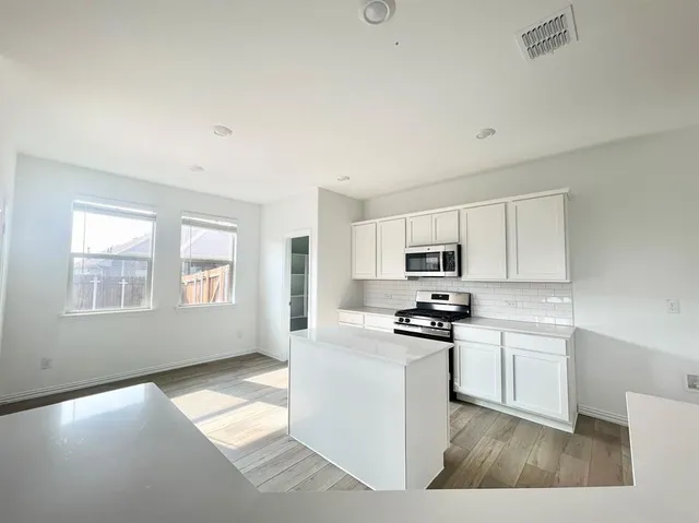 a kitchen with stainless steel appliances a stove a sink a refrigerator white cabinets and a window