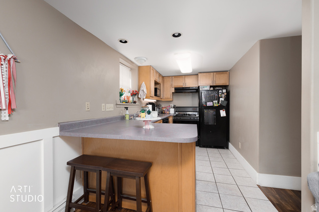 265 West 200 North Logan, UT 84321 - Photo 18 of 31 Kitchen with light tile patterned floors, black appliances, a peninsula, a breakfast bar area, and light countertops