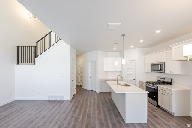 5287 South Acacia Drive, Unit 714 Mapleton, UT 84664 - Photo 11 of 21 Open-concept living space featuring wood-finish flooring, a contemporary kitchen with white cabinetry, stainless steel appliances, a kitchen island with pendant lighting, and an elegant staircase with black metal railings