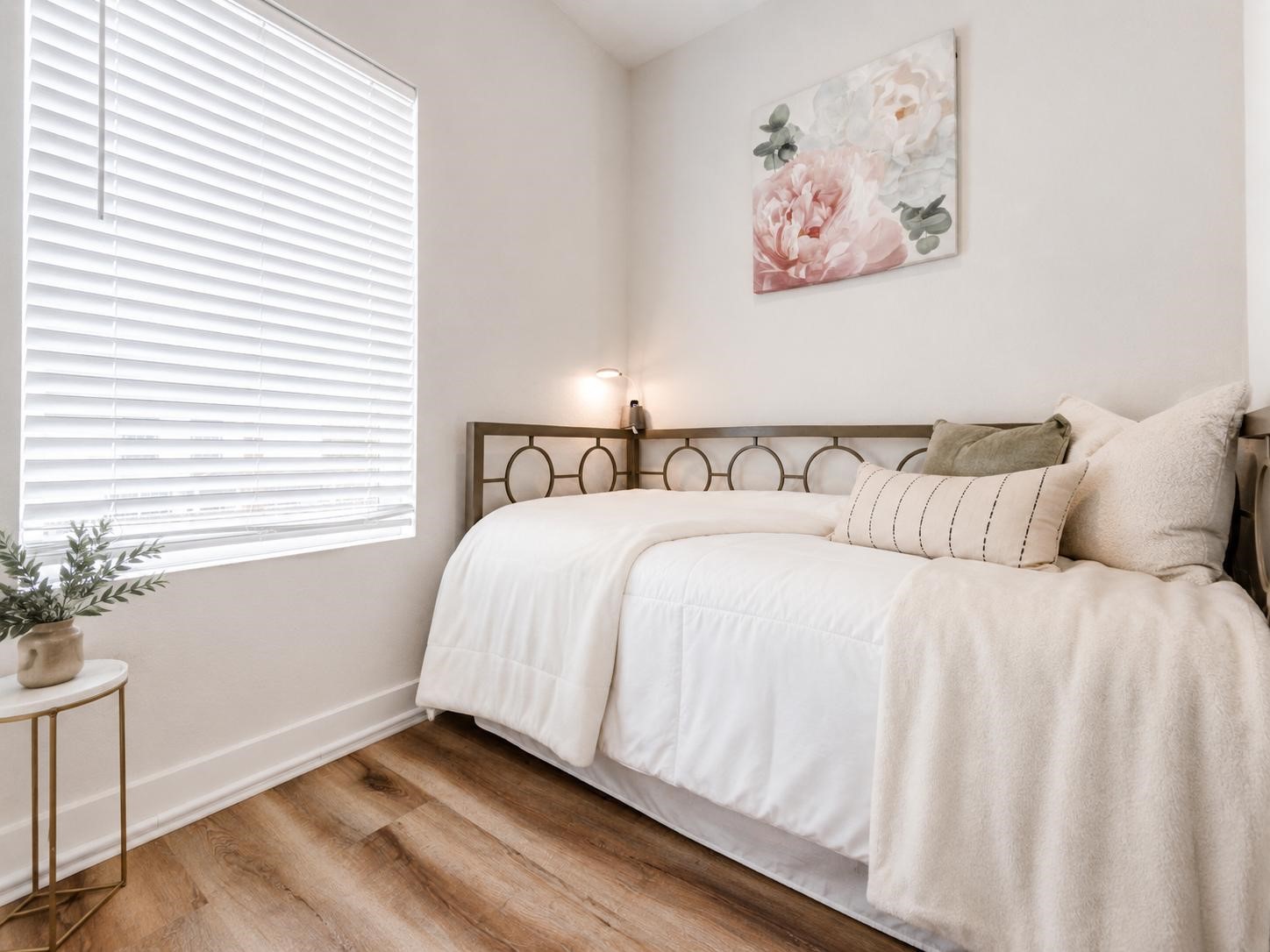 5407 Lee Street Houston, TX 77020 - Photo 7 of 17 This cozy bedroom features a daybed with a modern metal frame, soft white bedding, and warm wood flooring. A large window with blinds lets in natural light, while a floral artwork adds a touch of elegance. Perfect for a guest room or small bedroom.