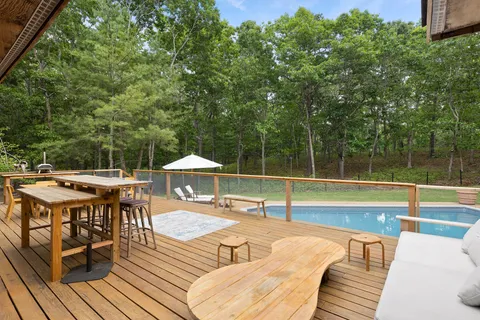 a view of a patio with couches table and chairs under an umbrella with wooden floor and fence
