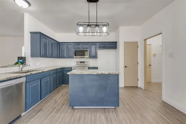 a large kitchen with stainless steel appliances granite countertop a stove refrigerator and a wooden floor