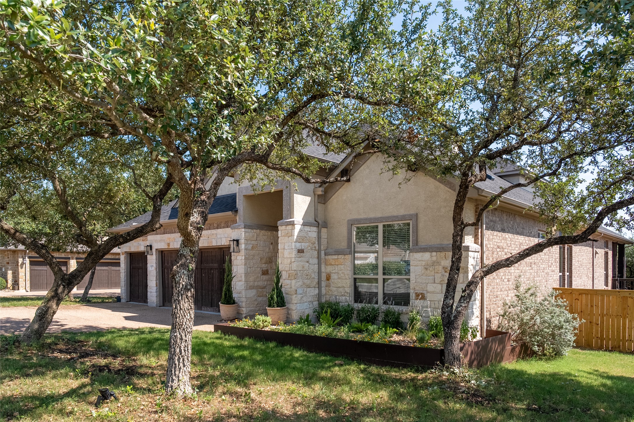 1225 Grassy Field Road Austin, TX 78737 - Photo 2 of 40 View of property hidden behind natural elements with stone siding, concrete driveway, stucco siding, and a garage