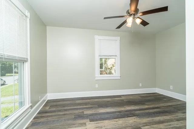 an empty room with wooden floor fan and windows