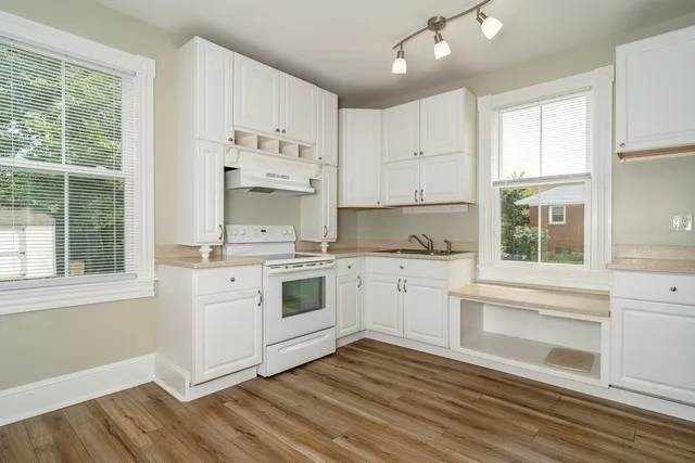 a kitchen with granite countertop white cabinets and white appliances with wooden floor