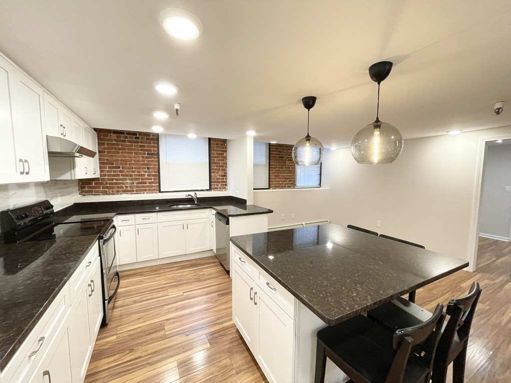 39 Hemenway Street, Unit 26 Boston, MA 02115 - Photo 1 of 27 a large kitchen with a stove a sink dishwasher a kitchen island with wooden cabinets and floor