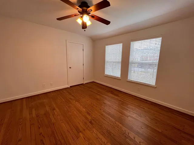 an empty room with wooden floor chandelier fan and windows