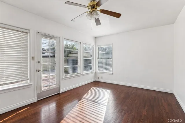 an empty room with wooden floor ceiling fan and windows