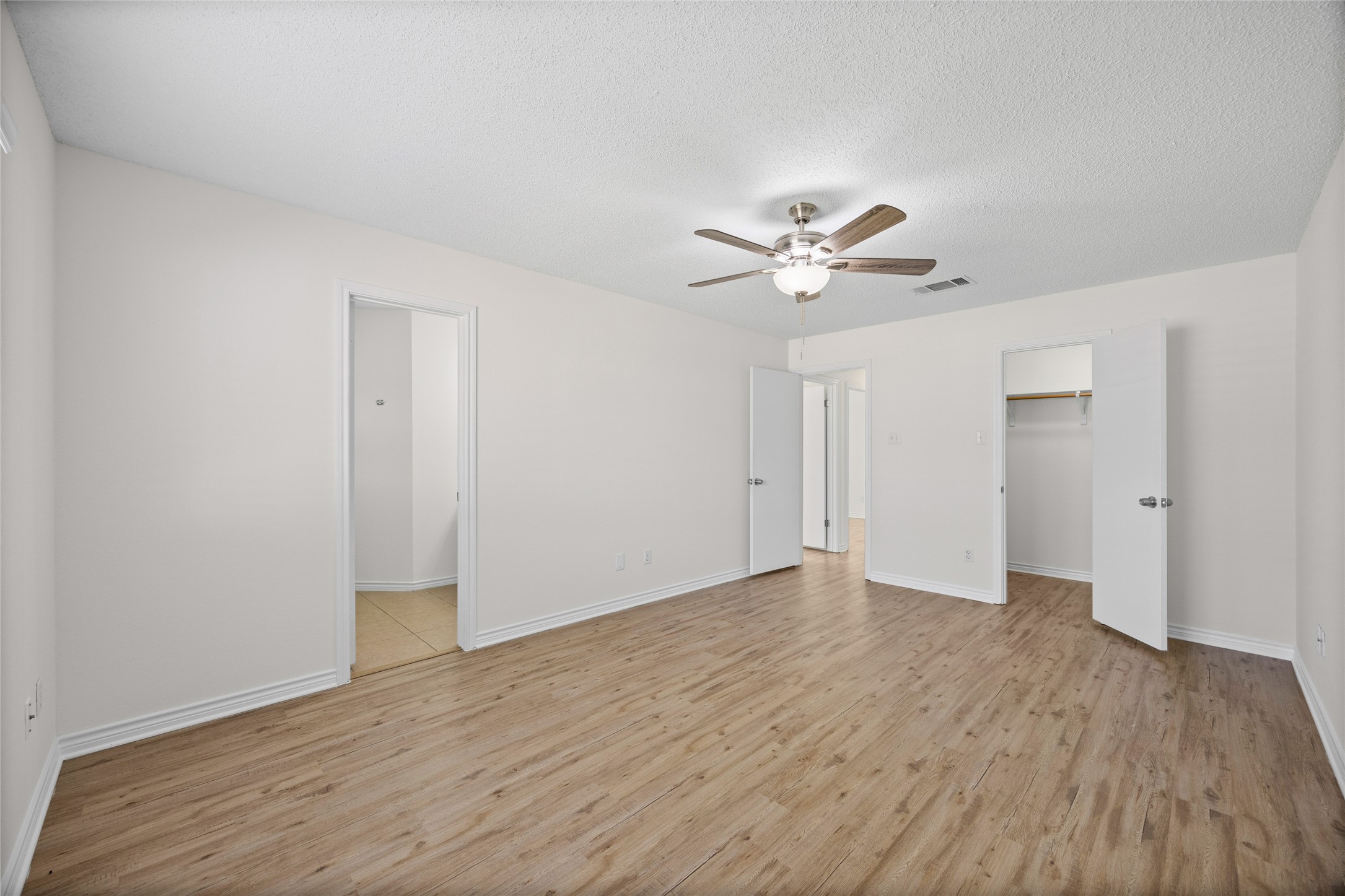 806 Calico Drive Austin, TX 78748 - Photo 19 of 25 Unfurnished bedroom with light wood-style floors, a walk in closet, a ceiling fan, and a textured ceiling