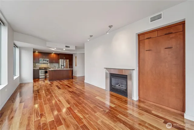 a view of an empty room with wooden floor and a kitchen