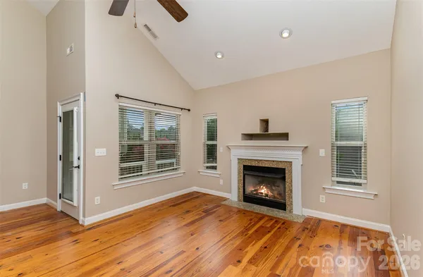 a view of an empty room with wooden floor fireplace and a window