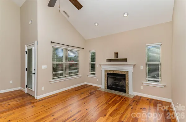a view of an empty room with wooden floor fireplace and a window