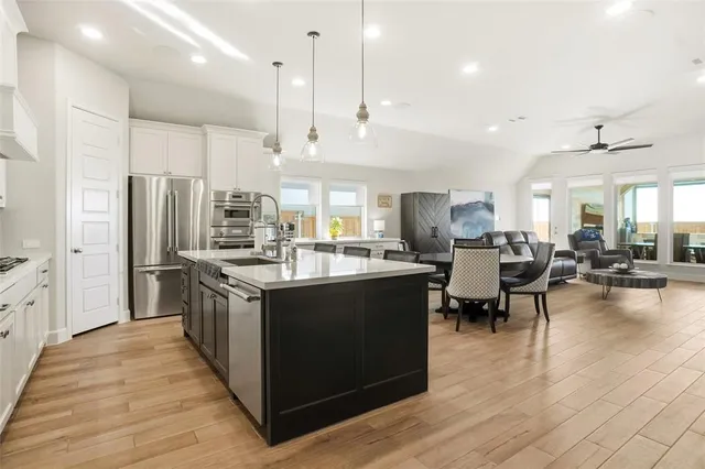 a kitchen with stainless steel appliances granite countertop a refrigerator a stove a sink dishwasher and a dining table with wooden floor