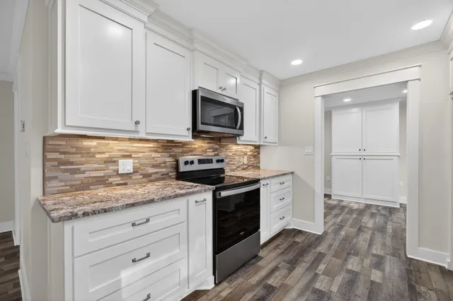 a kitchen with granite countertop stainless steel appliances white cabinets and a window