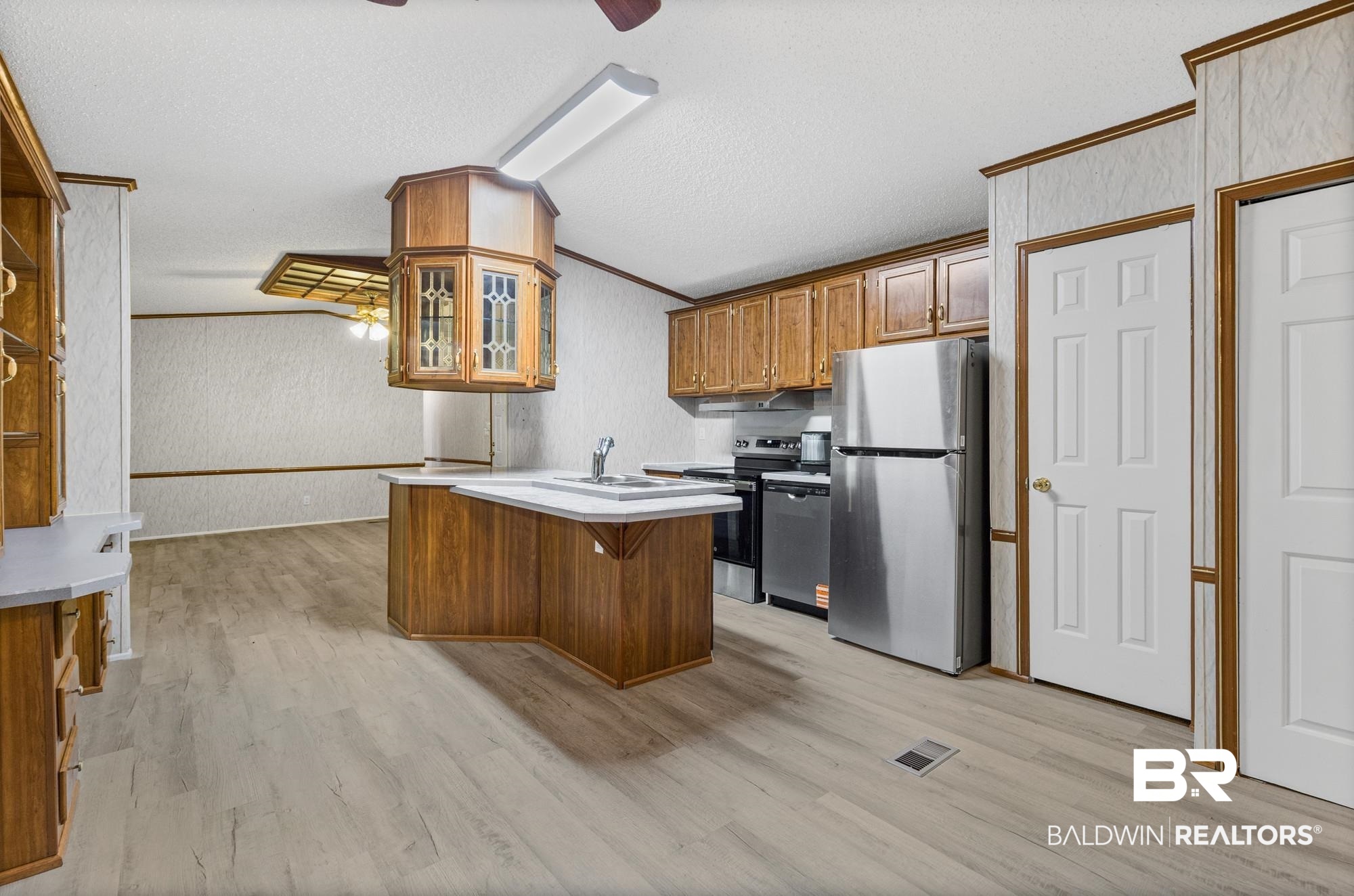 8675 Hunters Pointe Drive North Theodore, AL 36582 - Photo 5 of 20 Open-concept kitchen with wood-finish flooring, wood cabinetry, stainless steel appliances, and a central island with a sink