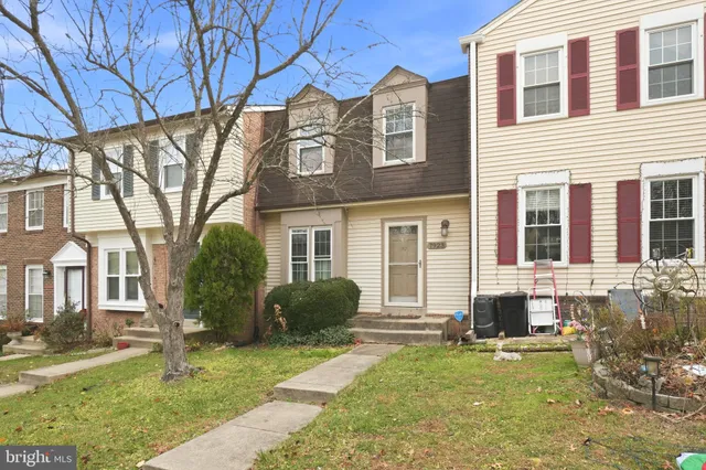 a view of a brick house with a yard plants and large tree