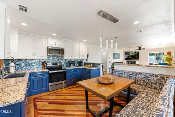 a kitchen with stainless steel appliances kitchen island granite countertop a sink dishwasher a stove and a refrigerator with wooden floor