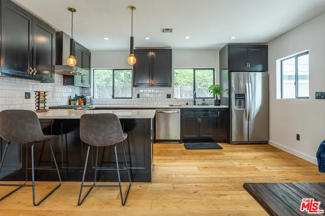 a kitchen with stainless steel appliances granite countertop a sink a stove a refrigerator and chairs