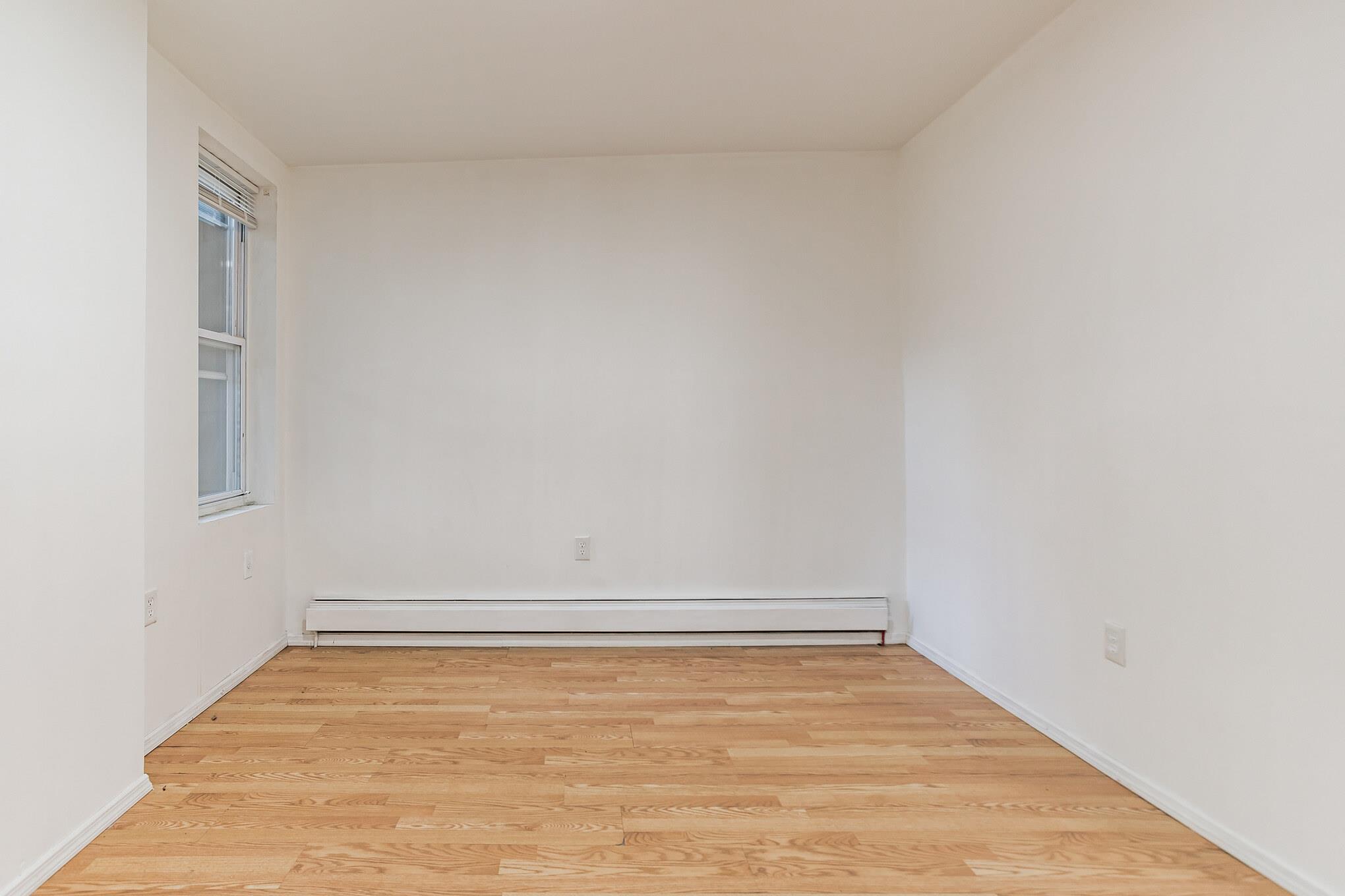2263 Ryer Avenue Bronx, NY 10457 - Photo 15 of 49 Spare room featuring a baseboard radiator and wood finished floors