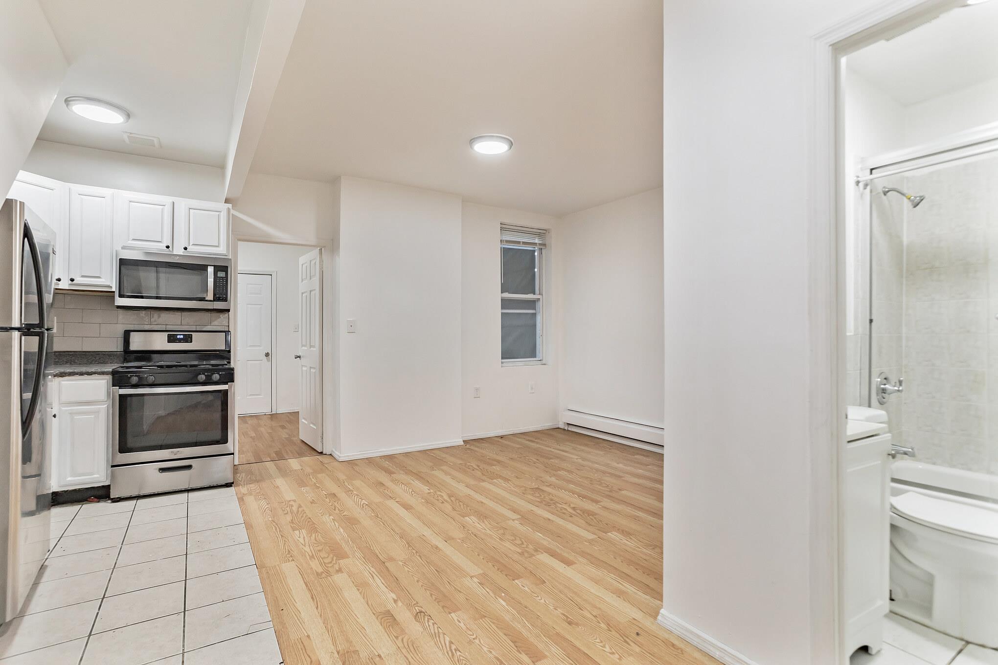 2263 Ryer Avenue Bronx, NY 10457 - Photo 8 of 49 Kitchen with stainless steel appliances, a baseboard heating unit, white cabinetry, dark countertops, and light wood-type flooring