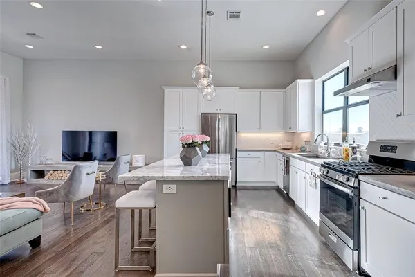 a kitchen with stainless steel appliances granite countertop a sink a stove a refrigerator and island with wooden floor