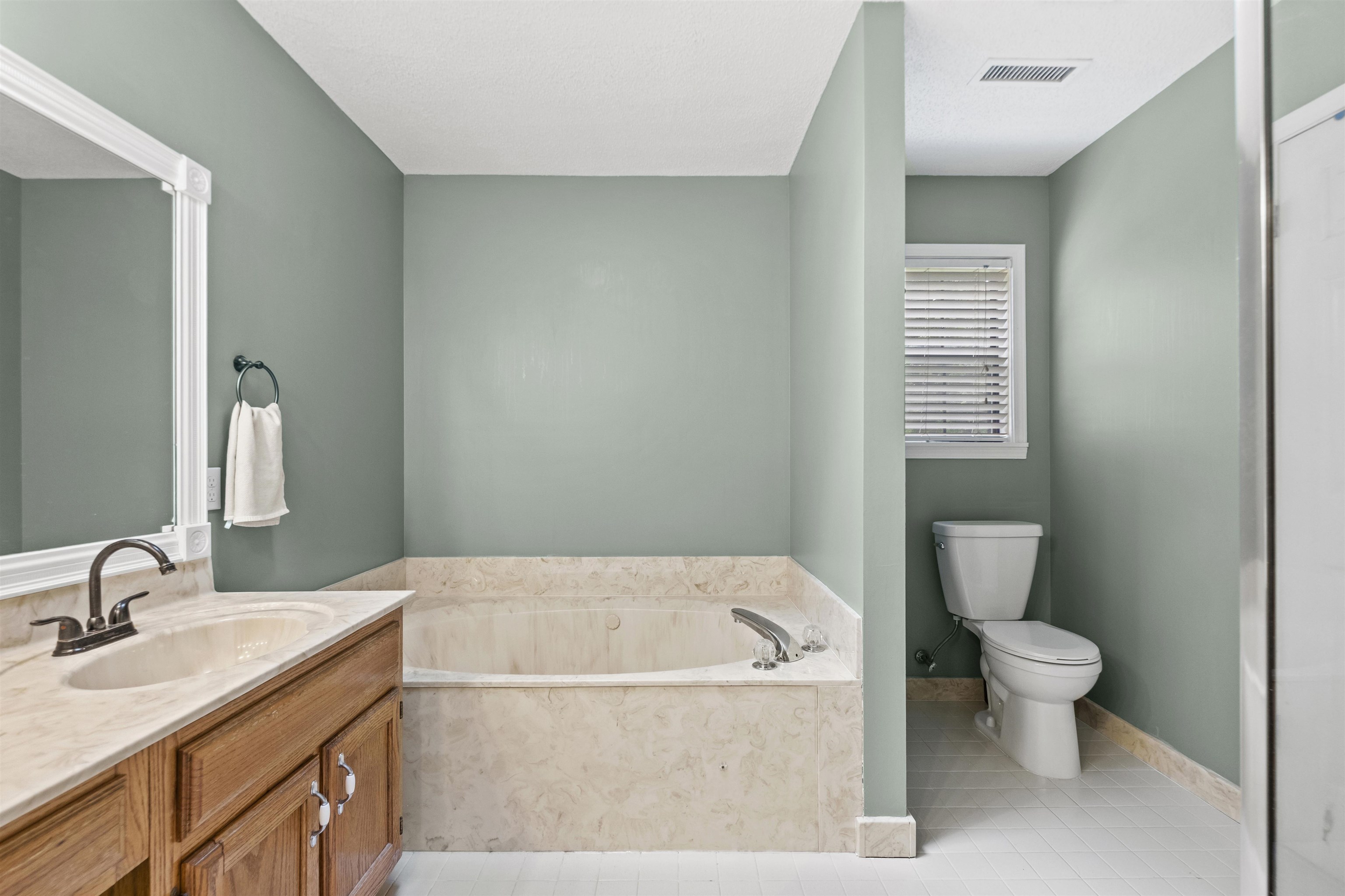 3601 Marshall Road Munford, TN 38058 - Photo 28 of 35 Bathroom featuring a built-in soaking tub with stone surround, a vanity with a double sink and stone countertop, a framed mirror, and a private water closet with a window
