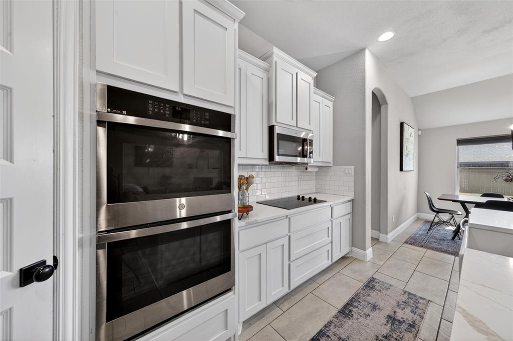 3245 Ribisl Lane Royse City, TX 75189 - Photo 8 of 39 Kitchen with stainless steel appliances, white cabinetry, vaulted ceiling, light stone countertops, and arched walkways