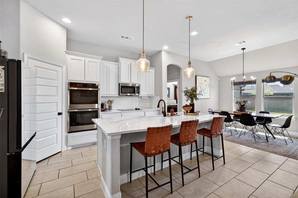 3245 Ribisl Lane Royse City, TX 75189 - Photo 9 of 39 Kitchen featuring black appliances, white cabinetry, a kitchen island with sink, a breakfast bar, and tasteful backsplash
