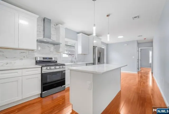 a kitchen with stainless steel appliances kitchen island granite countertop a sink a stove a refrigerator and white cabinets with wooden floor