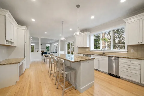 a kitchen with stainless steel appliances granite countertop a stove a sink dishwasher a refrigerator and white cabinets with wooden floor