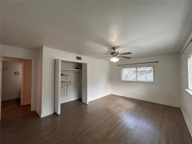 an empty room with wooden floor chandelier fan and windows